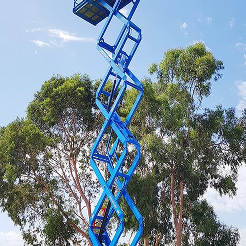 Blue rough terrain scissor lift extended on outdoor ground