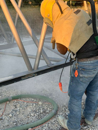 Blaster in protective hood cleaning structural steel